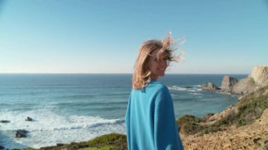 Mavi örgü süveter giyen bir kadının portresi uçurumun kenarındaki güçlü okyanus rüzgarında destansı deniz manzarasına bakıyor. Bin yıllık maceranın portresi. Mutlu ve heyecanlı bir kadın.