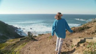 Sinema macera konsepti, genç özgür bir kadın sahil şeridi rüzgârlı sahilinde yolun sonuna ulaşır. Kadın güneşli bir yolculuk gününde hedefe ulaştıktan sonra kameraya bak.
