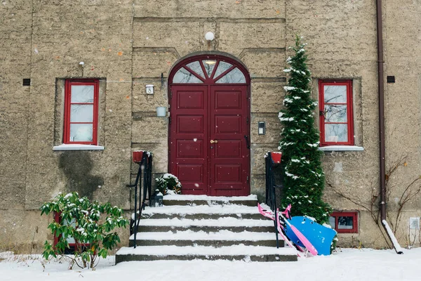 降雪中の美しい冬の日 住宅ビルへのカラフルな明るい赤いドアの入り口 スカンジナビアの都市の雪の日 居心地の良い 子供の雪のおもちゃやスライド — ストック写真