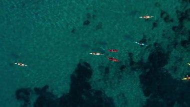 İspanya 'nın Mallorca kıyı şeridini keşfederken kayak grubu turunun hava çekimi. Kanocuların drone görüntüsü mercan resifleri ve turkuaz berrak mavi su üzerinde kürek çekiyor. Tatildeki aile için eğlenceli spor aktiviteleri