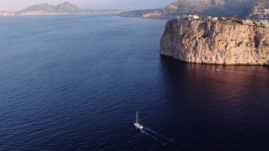 Destansı Mallorca uçurumunun sinematik hava dronu görüntüsü sonsuz mavi deniz ve okyanusu çevreledi. Lüks bir yat açık denizde yüzüyor. Mükemmel bir yaz tatili ve tatil yeri.. 