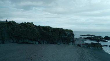 Sahilde kayalıklarda yürüyen bir adam silueti. İzlanda 'da seyahat yolculuğunda dengesiz macera titreşimleri