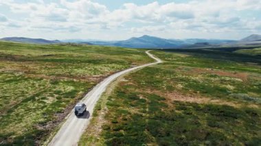 Arkasında yedek lastik ve çatıda güneş panelleri olan Macera Karavanı 'nın yan drone görüntüsü. 4x4 üstü kapalı araba sürüşü. Uzak, egzotik bir varış noktasında, dağ yaylalarında toprak kır yolunda.