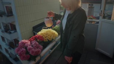 Genç bir kadın, gün batımında evinin balkonuna çiçek bırakıyor. Balkon çiçek yataklarında yetişen açık hava çiçeklerine bakıyorum. Bahçıvanlık hobisi 