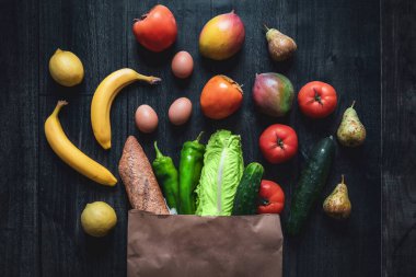 Ahşap arka planda sebze, meyve, yumurta ve ekmek dolu alışveriş torbası. Karanlık yemek fotoğrafçılığı. Temel gıda maddelerinin fiyatları yükseliyor
