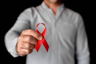 Kameraya Dünya AIDS Günü 'nü destekleyen kırmızı bir kurdele gösteren bir adam. HIV virüsüyle savaşmak