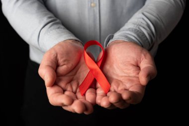 Dünya AIDS Günü 'nü desteklemek için iki eli açık kırmızı kurdele tutan bir adam. HIV hastaları için anlayış ve empati