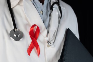 Göğsüne kırmızı kurdele takan bir doktorun yakın çekimi. Dünya AIDS Günü 'nün sembolü. HIV 'li kişilere sağlık personelinden destek. AIDS virüsüne karşı önlem ve mücadele