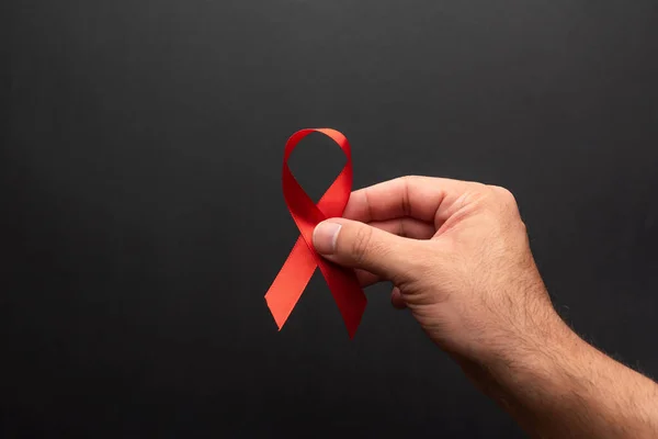 一只手拿着红丝带的男子的手 在黑色的背景上支持世界艾滋病日 12月1日 星期三 — 图库照片