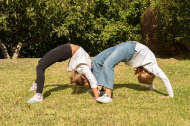 Parkta akrobatik egzersizler yapan iki kız. Çocuklar dışarıda oynuyor ve jimnastik aktivitelerine katılıyorlar. Gençlikte sağlıklı yaşam ve beslenme