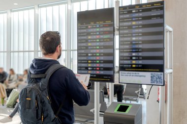 Havaalanındaki adam uçuş bilgilerine bakıyor. Uçuşlar iptal edildi. Bilgi noktası