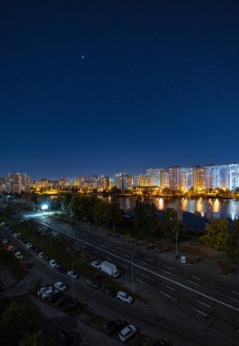 Yıldızlı gökyüzünün altındaki büyük şehrin gece manzarası. Müthiş parlak, sokağa çıkma yasağında çok renkli ışık var. Yatak odası civarındaki apartmanlar. Kyiv, Ekim 2022 'de. Ukrayna.