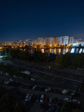 Yıldızlı gökyüzünün altındaki büyük şehrin gece manzarası. Müthiş parlak, sokağa çıkma yasağında çok renkli ışık var. Yatak odası civarındaki apartmanlar. Kyiv, Ekim 2022 'de. Ukrayna.