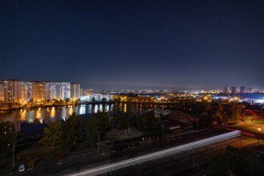 Yıldızlı gökyüzünün altındaki büyük şehrin gece manzarası. Müthiş parlak, sokağa çıkma yasağında çok renkli ışık var. Yatak odası civarındaki apartmanlar. Kyiv, Ekim 2022 'de. Ukrayna.