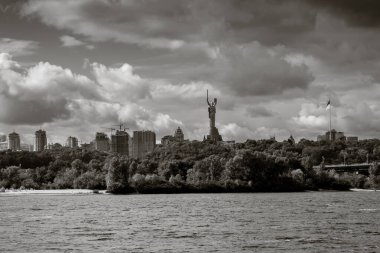 Gün batımında geniş nehrin üzerindeki tepelerin üzerindeki büyük şehir manzarası. Anavatanın Anavatanı ve Ukrayna bayrağıyla en yüksek bayrak direğine bakın. B & W fotoğrafı. Kyiv. Ukrayna.