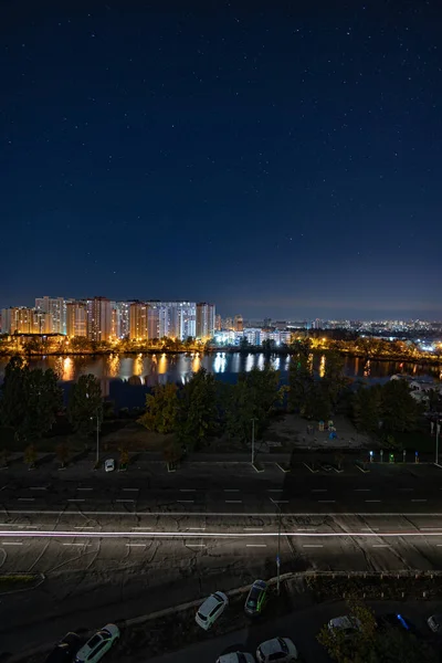 Yıldızlı gökyüzünün altındaki büyük şehrin gece manzarası. Müthiş parlak, sokağa çıkma yasağında çok renkli ışık var. Yatak odası civarındaki apartmanlar. Kyiv, Ekim 2022 'de. Ukrayna.