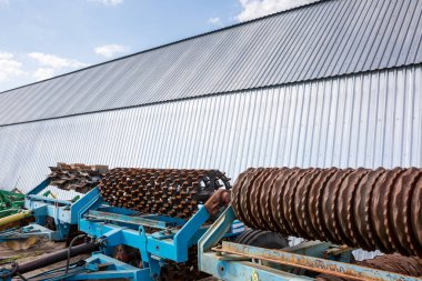 Ekinler için eski disk harrow, tarım işletmesinin maddi ve teknik temelinde kemer hangarının yanında duruyor. Ukrayna 'nın orta kesimindeki tarım işletmeleri.