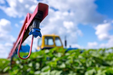 An old farm tractor painted in yellow-blue color with a trailed sprayer with tank capacities is preparing to spray a crop protection product on a field sown with sunflowers. clipart