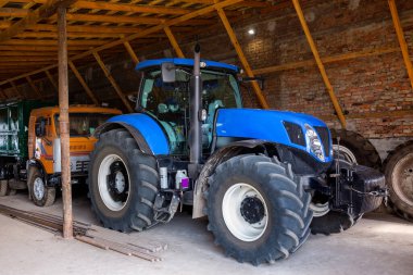 Yeni bir modern mavi traktör bir çiftlik hangarında park halinde..