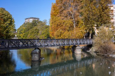 İtalya 'nın Torino kentindeki Dora Riparia nehrinin üzerindeki Ponte del Carbone (Kömür Köprüsü) sonbahar manzarası. Renkli yapraklar suya yansıyor.
