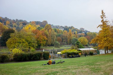 Parco del Valentino, Torino, İtalya 'da sonbahar, canlı sonbahar yapraklarıyla. İnsanlar Po Nehri yakınlarındaki çimlerde dinleniyor..