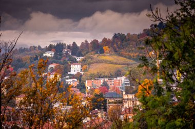 İtalya, Torino 'daki tepe manzarası sonbahar renkleriyle dolup taşıyor. Evler bulutlu bir gökyüzünün altındaki manzarayı noktalar..