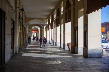 Torino, İtalya - 08 Kasım 2021: Yayalar, Romanlar üzerinden uzanan kemerli portikolar altında yürürken, dükkanlar ve güneş ışığı yürüyüş yoluna gölge düşürüyor