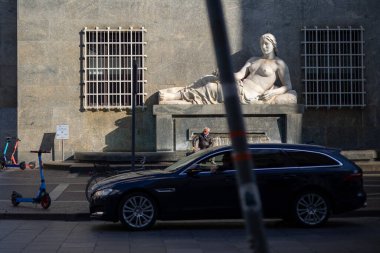 Torino, İtalya - 08 Kasım 2021: Fontana della Dora ön planda arabalı ve scooterlı bir binanın ön cephesine yaslanmış çıplak bir heykel yer alıyor