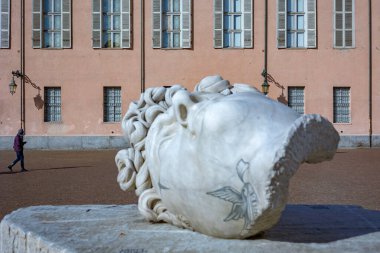 Torino, İtalya - 08 Kasım 2021: Apollo 'yu Michelangelo tarzında tasvir eden mermer başlıklı heykel, modern dövme benzeri işaretler içeriyor, Piazzetta Reale' de arka planda Kraliyet Sarayı ile birlikte sergileniyor ve yanından geçen bir kişi