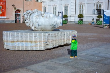 Torino, İtalya - 08 Kasım 2021: Genç bir çocuk, Apollo 'yu Michelangelo tarzında tasvir eden, modern dövme benzeri dövmeler içeren, Torino Kraliyet Sarayı yakınlarındaki Piazzetta Reale' de sergilenen mermer başlı heykele dikkatle bakıyor