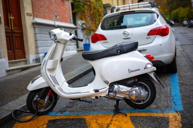 Torino, İtalya - 08 Kasım 2021: Beyaz bir Vespa S 125 scooter bir şehir caddesinde belirlenmiş park yerine park edilmiş, arkasında beyaz bir Opel Astra arabasının arka koltuğunda