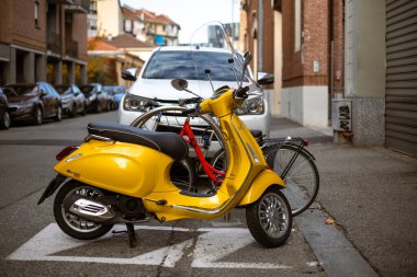 Torino, İtalya - 08 Kasım 2021: Sarı bir Vespa Primavera Sprint 125, bir şehir caddesinde belirlenmiş park yerine park etmiş bir scooter, bisikletler ve yakınındaki park edilmiş araçlar