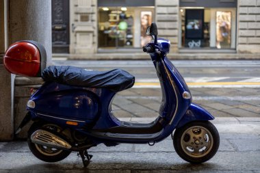 Torino, İtalya - 10 Kasım 2021: Mavi bir Vespa LX 150 scooter ve kırmızı kapaklı bir çanta mağaza önlerine park edilmiş.