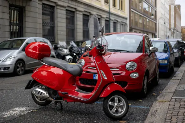 Torino, İtalya - 10 Kasım 2021: Ön camlı kırmızı Vespa Primavera scooter ve park halindeki arabalı kırmızı top çanta