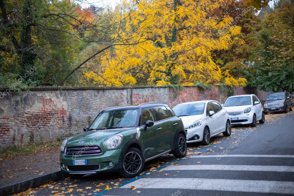 Turin, Italy - Nov 08 2021: A dark green Mini Countryman parked on a city street covered with fallen autumn leaves, alongside other parked cars under autumn foliage