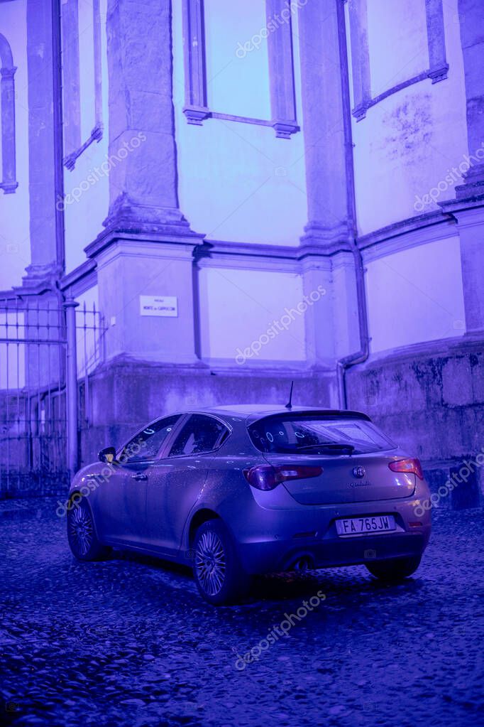 Turin, Italy - Nov 08 2021: A dark-colored Alfa Romeo Giulietta parked on a cobblestone street near a building with architectural details under a nighttime or twilight sky