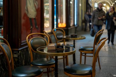 Torino, İtalya - 9 Kasım 2021: Kafe hattının dışındaki boş masa ve sandalyeler, arka planda insanların bulunduğu ve masalarda Lavazza markalı şeker paketlerinin yer aldığı kapalı bir yürüyüş yolu.