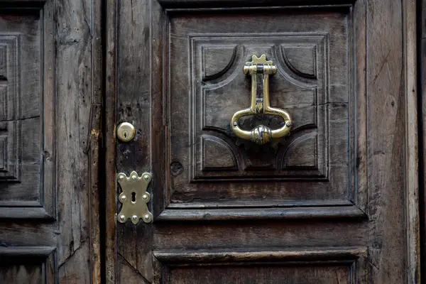 Karanlık, yıpranmış ahşap bir kapıya yakın plan. Dekoratif el yapımı pirinç kapı tokmağı anahtar şeklinde..