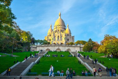 Paris, Fransa - 9 Kasım 2011: Montmartre tepesindeki Sacre-Ceour Bazilikası, Romano-Bizans mimari harikası. Ziyaretçiler çimlerde ve merdivenlerde dinleniyor, bu ikonik simgenin güneşli manzarasının tadını çıkarıyorlar..