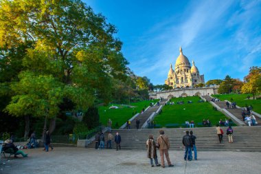 Paris, Fransa - 9 Kasım 2011: Montmartre tepesindeki Sacre-Ceour Bazilikası, Romano-Bizans mimari harikası. Ziyaretçiler çimlerde ve merdivenlerde dinleniyor, bu ikonik simgenin güneşli manzarasının tadını çıkarıyorlar..