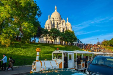 Paris, Fransa - 9 Kasım 2011: Montmartre Hill 'deki Sacre-Ceour Bazilikası. Ziyaretçiler basamaklarda oturur, patika boyunca yürür ve güneşli bir günde yeşil alanlarla çevrili bir turist trenine biner..