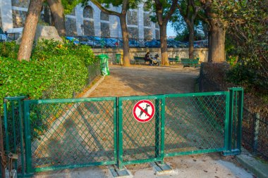 Paris, Fransa - 9 Kasım 2011: Yeşil metal kapılı bir parkta çitlerle çevrili bir bölüm. Kapıdaki işaret köpeklere izin verilmediğini gösteriyor. Bölgeyi çevreleyen sıralar ve ağaçlar.