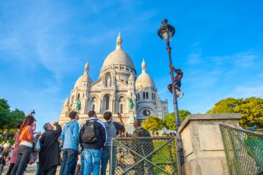 Paris, Fransa - 09 Kasım 2011: Bir kişi Sacre-Ceour Bazilikası 'nın önündeki bir sokak lambasına tırmanıyor, açık mavi gökyüzü altında ikonik mimarinin keyfini çıkaran bir kalabalıkla çevrili..