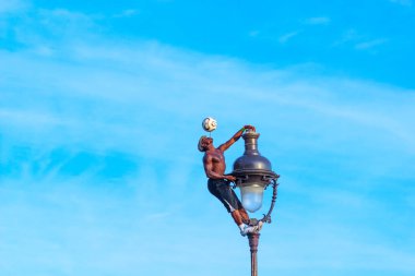 Paris, Fransa - 9 Kasım 2011: Iya Traore bir Paris lambasına asıldı, bir futbol topunu ayaklarıyla ustalıkla dengeledi açık mavi gökyüzü ile ince bulutlar arasında.