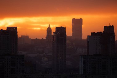 Puslu bir günbatımı Kyiv siluetini sıcak, altın renkli, siluetli binalar ve Kyiv Pechersk Lavra 'nın çan kulesi altında yıkıyor..
