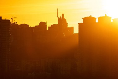 Bulanık bir günbatımı Kyiv siluetini sıcak, altın renkli, siluetli binalar ve Anavatan Anıtı 'nın siluetinde yıkıyor..