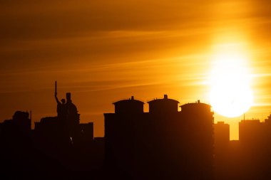 Kyiv silueti alacakaranlık renklerine karşı siluetlendi. Anavatan Anıtı solda görünüyor ve şehir ışıkları aşağıdaki karanlığı aydınlatmaya başlıyor..
