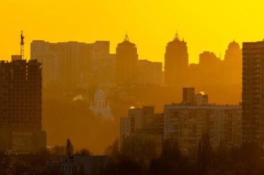 Alacakaranlıkta Kyiv siluetinde Berezniaky ilçesi ön planda, Pechersk tepeleri sağ kıyıda solan ışığa karşı ayırt edilebilir.