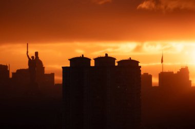 Anavatan Anıtı 'nın ve Ukrayna bayrağının belirgin bir şekilde dalgalandığı uzun bir bayrak direğinin yer aldığı Kyiv silueti üzerinde dramatik bir günbatımı..