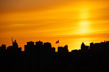Anavatan Anıtı 'nın ve Ukrayna bayrağının belirgin bir şekilde dalgalandığı uzun bir bayrak direğinin yer aldığı Kyiv silueti üzerinde dramatik bir günbatımı..